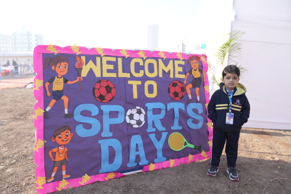 A young student standing next to a colorful "Welcome to Sports Day" handmade poster at a Pencilpod Preschool event.