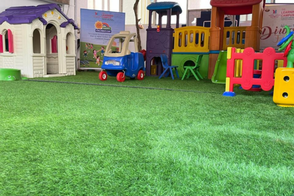 Safe outdoor play area at Pencilpod Preschool in Wakad with colorful toy houses, a slide, and artificial green grass.