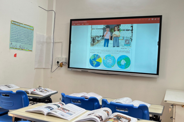 A digital interactive smart board in a classroom with desks and open textbooks.