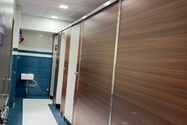 Clean and modern school restroom with wooden-finish partitions and a small white sink.