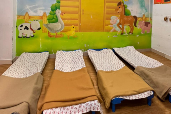 Four small floor beds with blankets in a preschool nap room featuring a colorful animal mural on the wall.